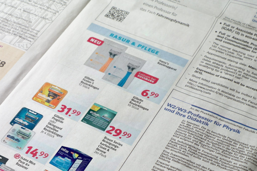 Werbeanzeige in einer Zeitung für Rasurprodukte, darunter Gillette und Harry's Rasierapparat, der exklusiv bei Rossmann erhältlich ist.