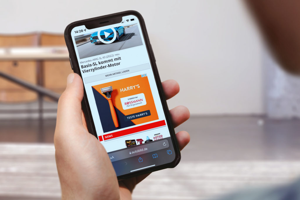 Eine Hand hält ein Smartphone, auf dem eine Webseite mit einem Werbebanner für Harry's Rasierer angezeigt wird.