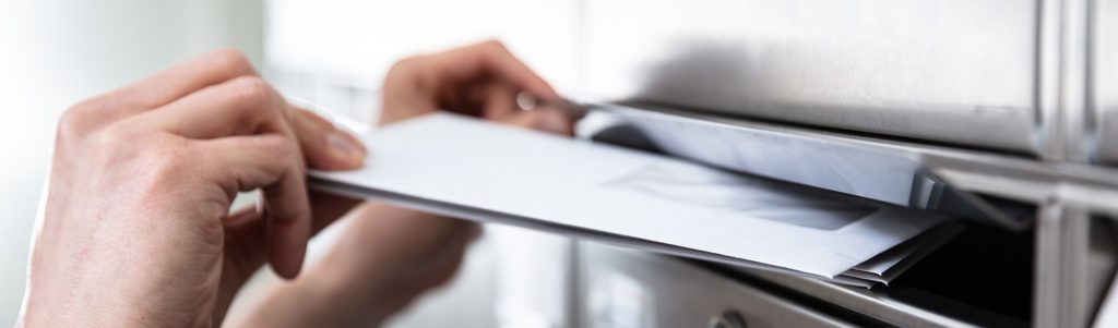Person steckt einen weißen Brief in einen Briefkasten.