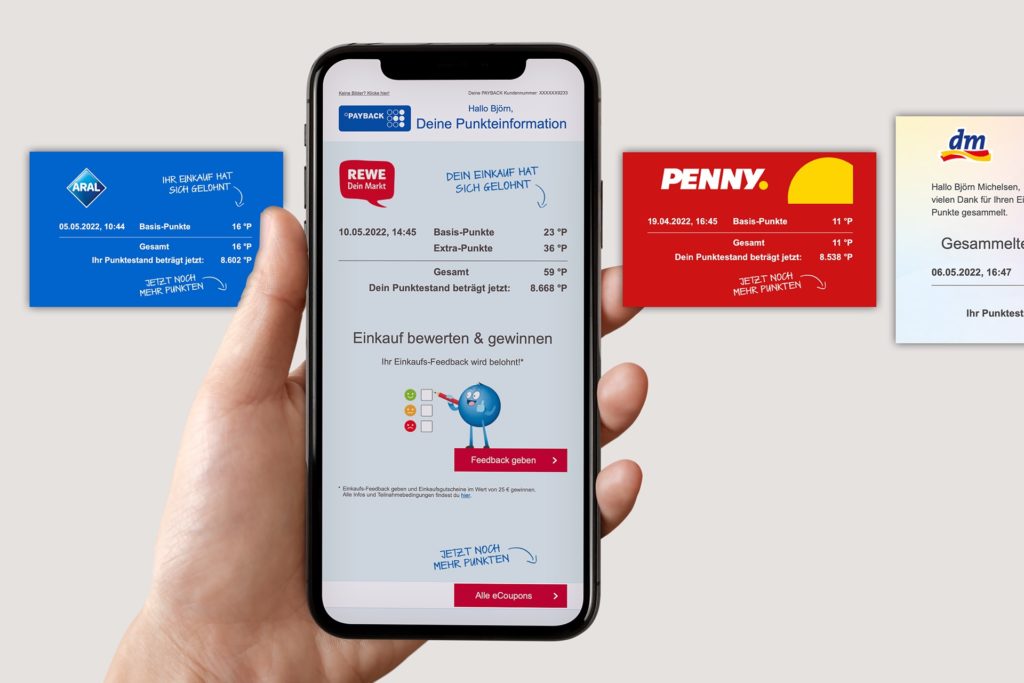 Eine Hand hält ein Smartphone, das eine PAYBACK-Punkteübersicht für einen Einkauf bei REWE anzeigt. Um das Smartphone herum sind weitere Punkteinformationen für Einkäufe bei Aral, Penny und dm dargestellt.