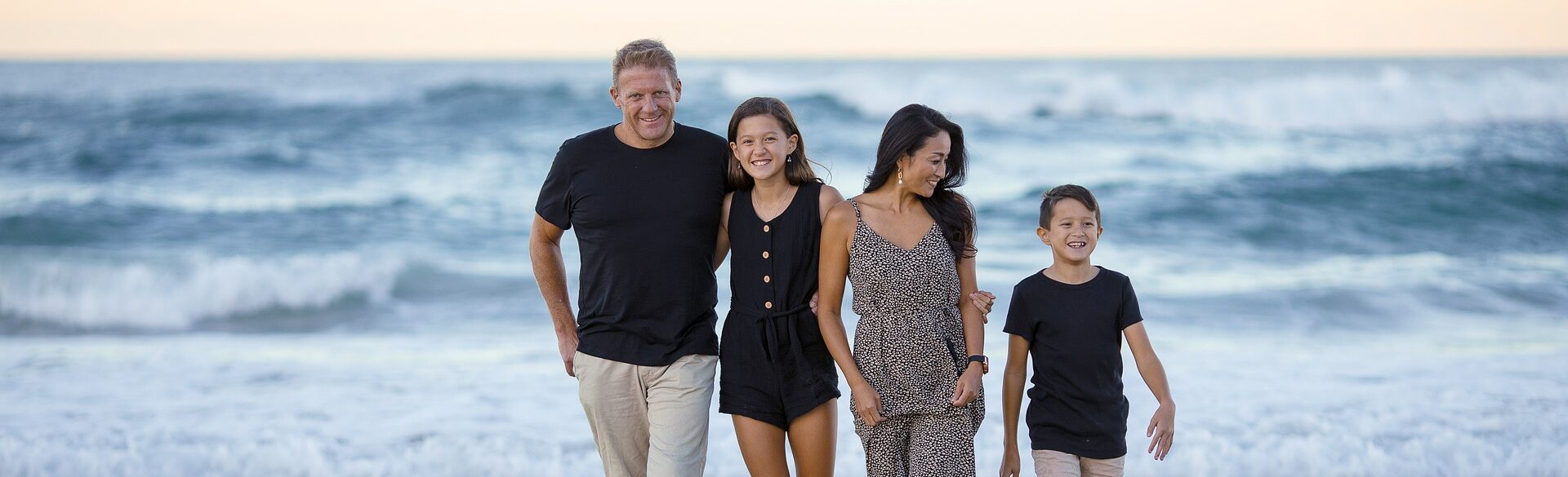 Familie (Vater, Mutter, Tochter und Sohn) im Sommer am Strand vor einem Ozean.