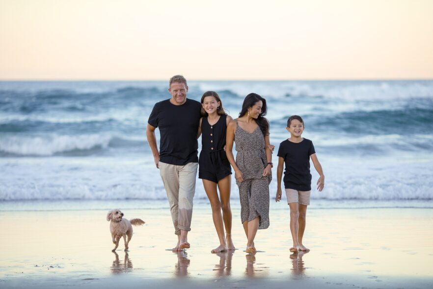 Familie (Vater, Mutter, Tochter und Sohn) im Sommer am Strand vor einem Ozean.